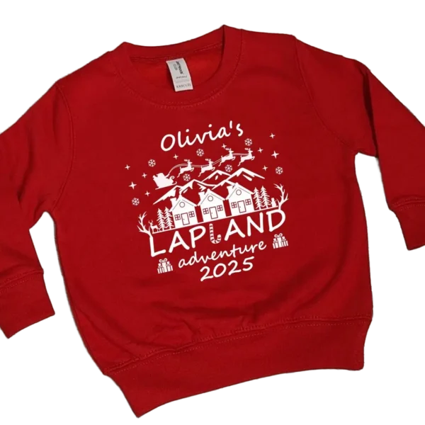 Red personalised Lapland Christmas sweatshirt with sparkly white vinyl showing Olivia's name, winter village, Santa's sleigh and 2025 adventure text